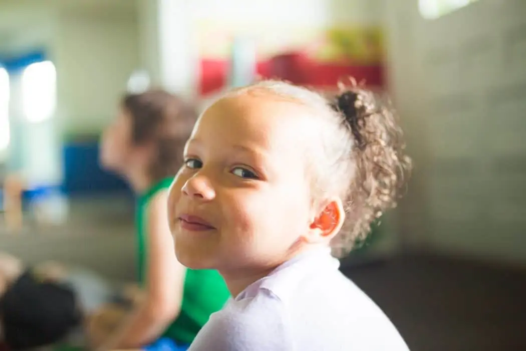 Young African American girl in preschool classroom smiling at camera. 
