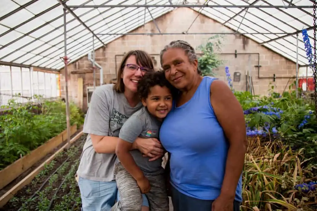 Two women and a child stand in green house at a urban farm. 
