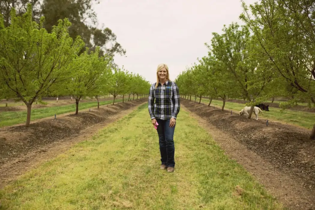 Woman standing at an almond farm discussing pollinators and how they play a role on the farm.