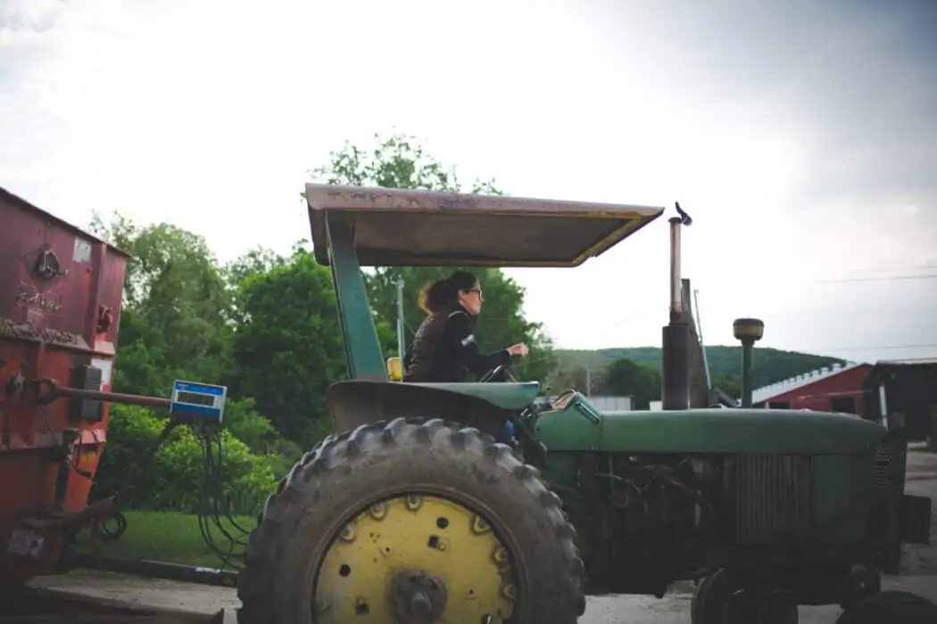 A woman driving a John Deere tractor on a dairy. 