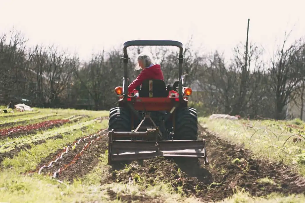 Woman driving a red tractor tilling the field